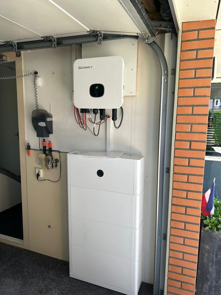 Omvormer en thuisaccu naast elkaar aan een garagemuur, geinstalleerd door Warmte Zon